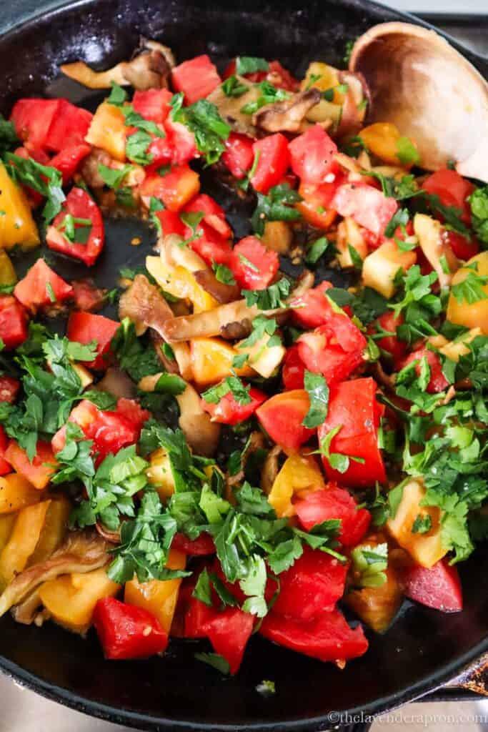 Adding fresh diced tomatoes to the mushrooms in a cast iron skillet.