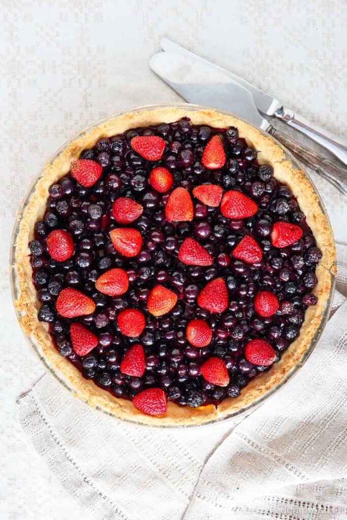 Blueberry Strawberry Pie overhead view on linen tablecloth with silver pie server.