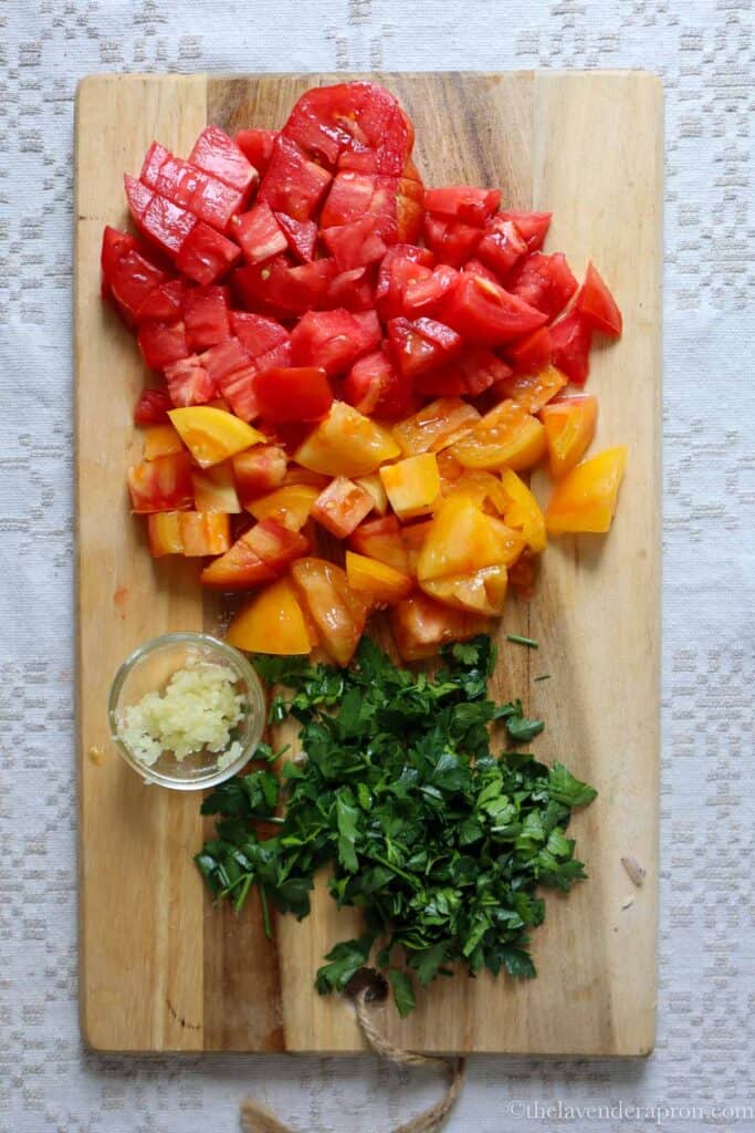 Diced tomatoes, minced garlic and chopped parsley on wooden board.