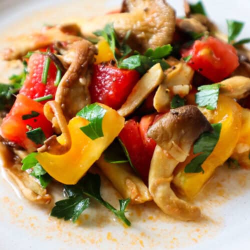 Sauteed Oyster mushrooms with tomatoes and parsely on a beige plate.