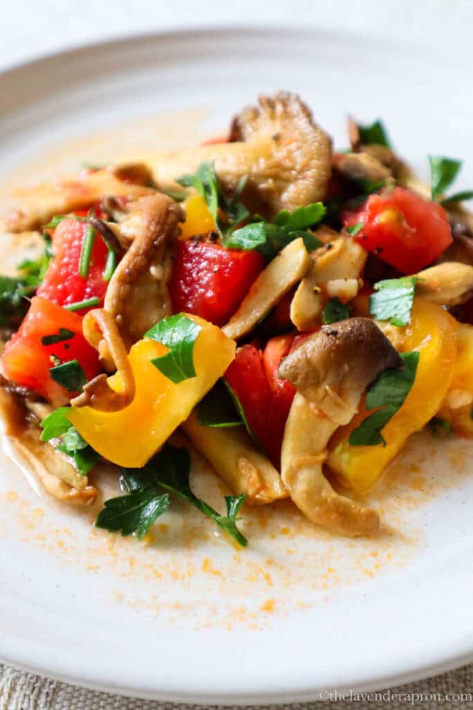 Sauteed Oyster mushrooms with tomatoes and parsely on a beige plate.