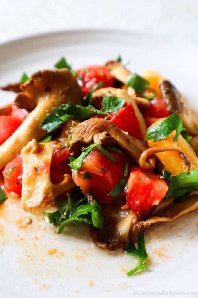 Sauteed tan oyster mushrooms with tomatoes and parsley on a beige plate.