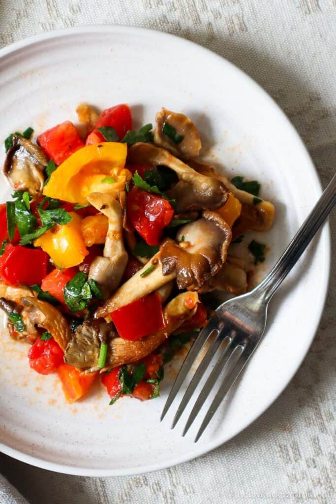 The best oyster mushroom recipe with diced tomatoes and parsley served on a beige plate with a fork.