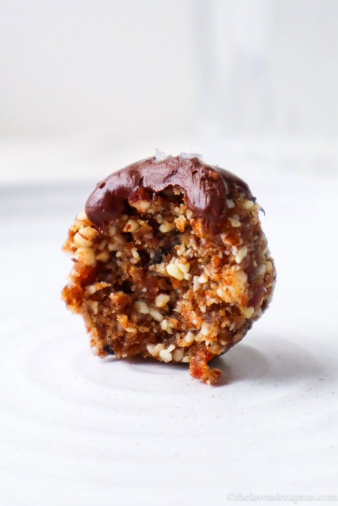 White plate with a date almond energy ball topped with dark chocolate and a pinch of sea salt with a bite taken out of it.