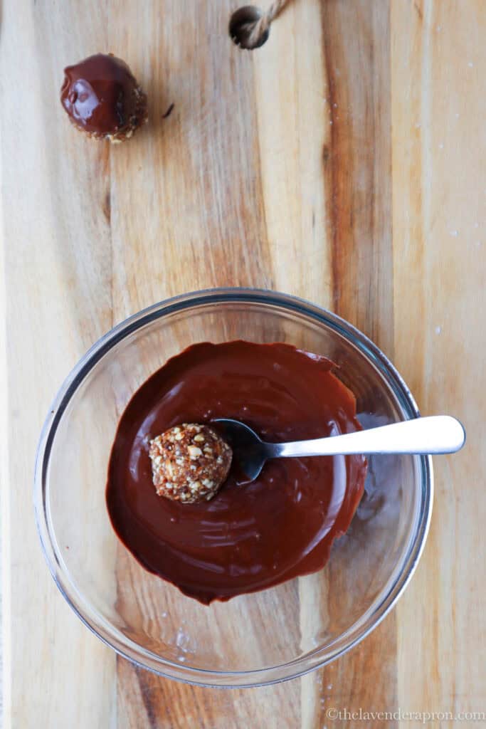 Dipping the date almond energy ball into the melted chocolate using a spoon.