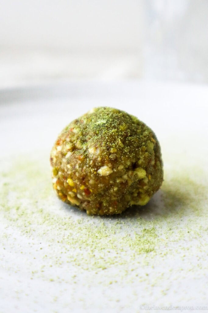Matcha energy ball with pistachio on a plate with a dusting of matcha powder.