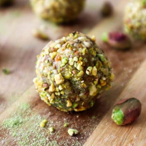 Matcha energy balls rolled in ground pistachios on a wooden board.