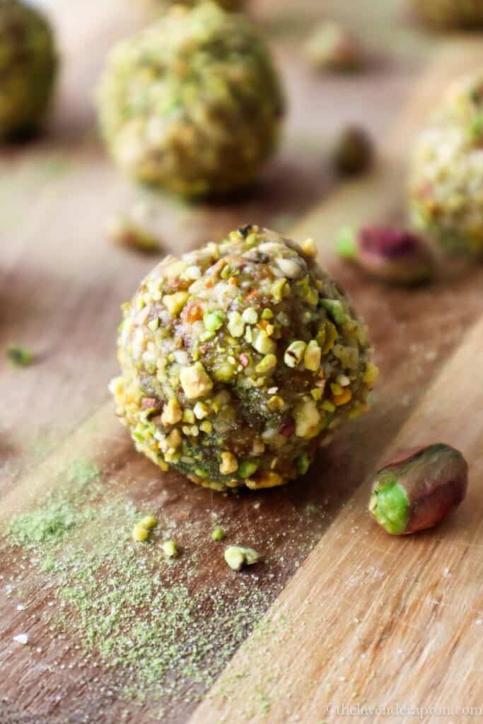Matcha energy balls rolled in ground pistachios on a wooden board.