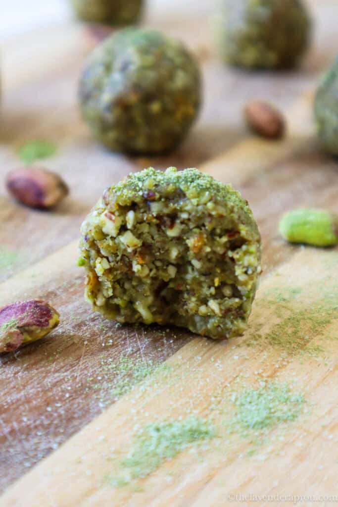 Pistachio bliss ball cut in half to show inside which has little bits and not completely smooth. It is covered with matcha powder on a wooden board.