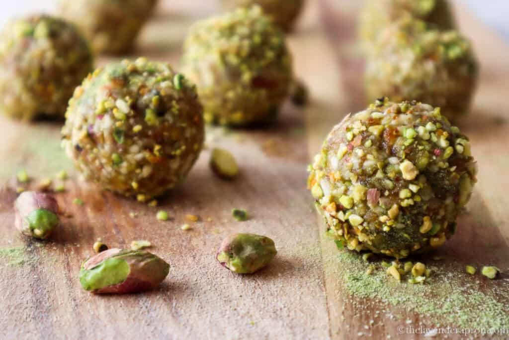 Matcha pistachio bliss balls on a wooden board with some scattered pistachios as well.
