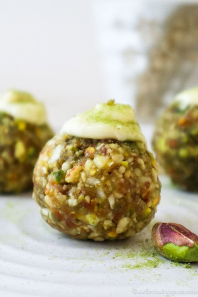 Pistachio matcha energy balls topped with white chocolate on a beige plate with a cup of coffee in the background.