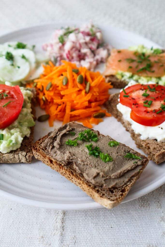 Baltic savory breakfast plate with chicken liver pâté on rye bread, creamy cucumber salad, carrot salad, radish salad, cottage cheese and tomato on rye bread and smoked salmon and avocado on bread.
