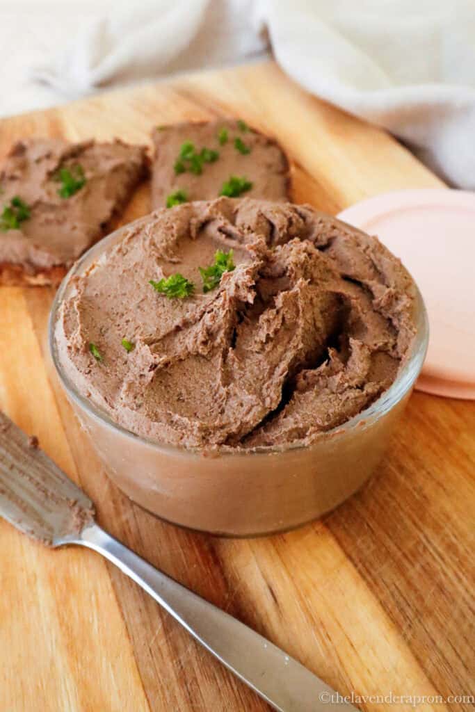 easy chicken liver pâté in a glass jar with dark rye bread on a wooden board.