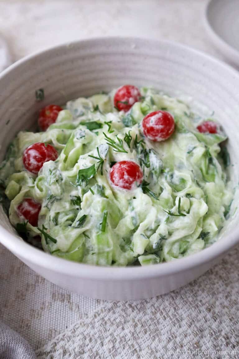 French cucumber salad topped with cherry tomatoes and herbs in beige bowl.