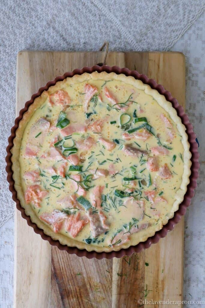 Pouring the egg mixture evenly over the salmon and spinach in the quiche pan.