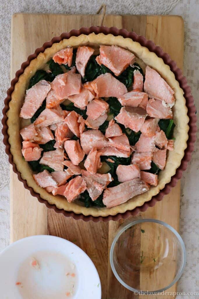 Pie crust with spinach and then salmon chunks scattered on top.