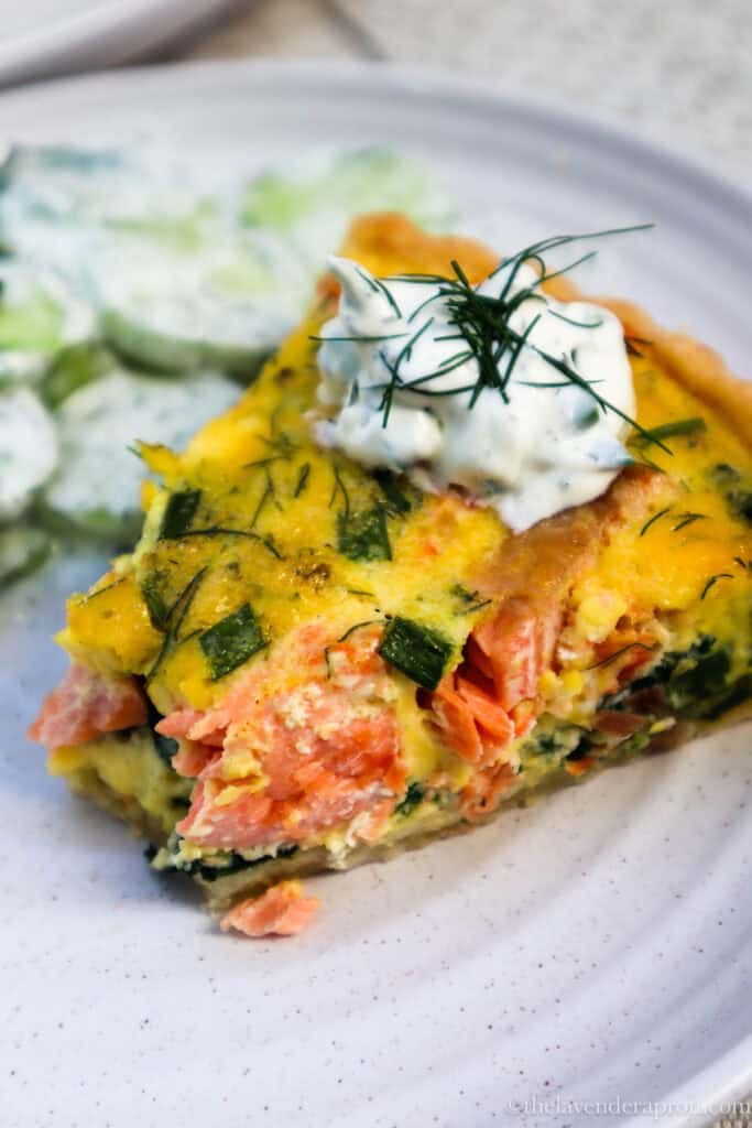 Salmon spinach quiche served with a dollop of cream and fresh herbs and with a side of cucumber salad.