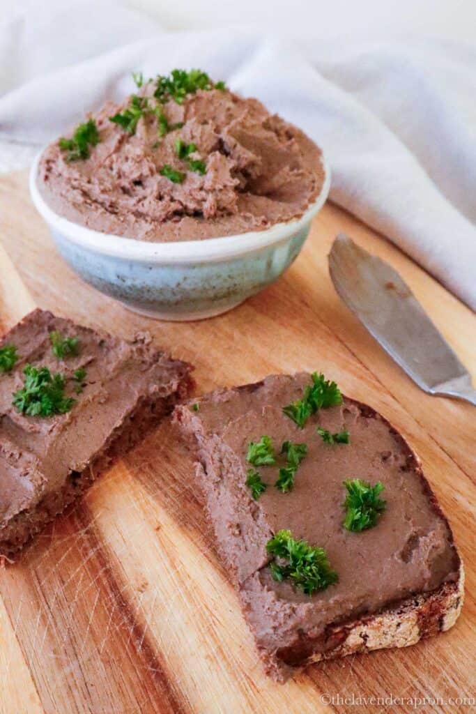 Simple chicken liver pate spread on dark rye bread on a wooden board.