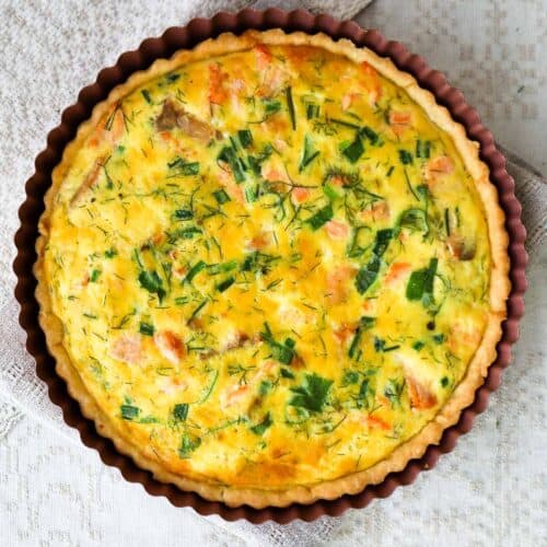 Baked salmon spinach quiche on linen potholder placed on a linen tablecloth.