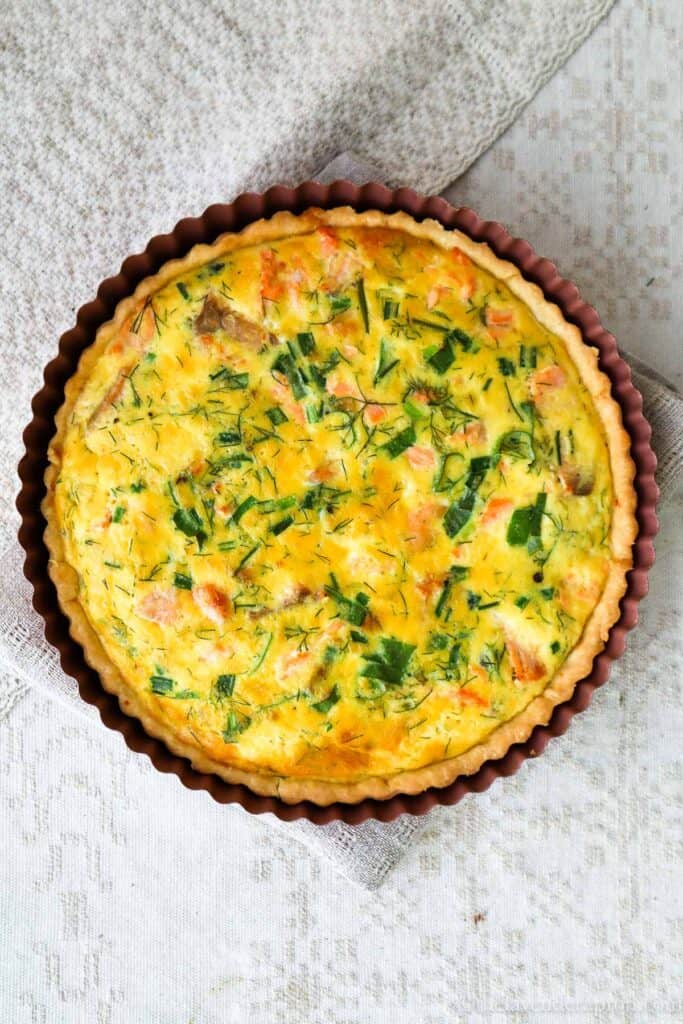 Baked salmon spinach quiche on linen potholder placed on a linen tablecloth.
