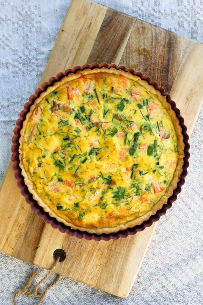 Salmon spinach quiche in a pink tin placed on a wooden chopping board to cool.
