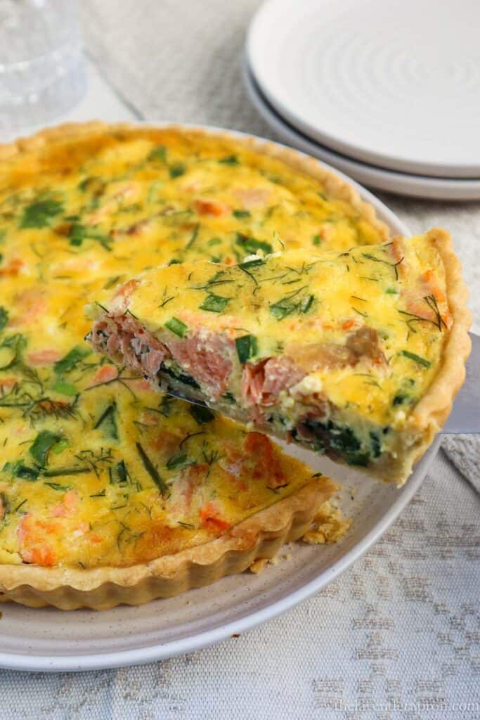 Slice of salmon spinach quiche held out with a spatula.