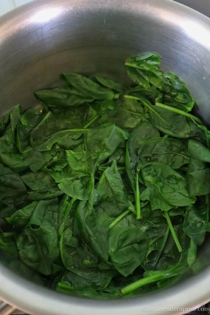 Wilting the baby spinach in a pot with just a touch of water until it is barely wilted.