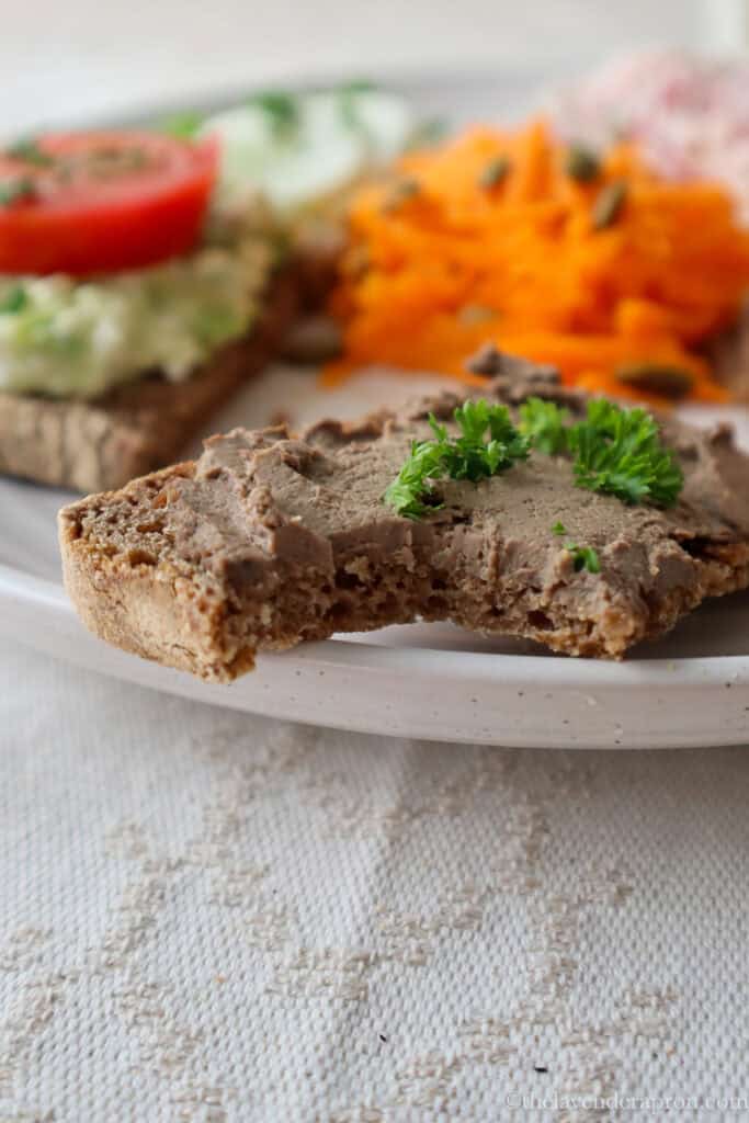 A bite taken out of a rye open-faced sandwich with a slather of chicken liver pate on top.