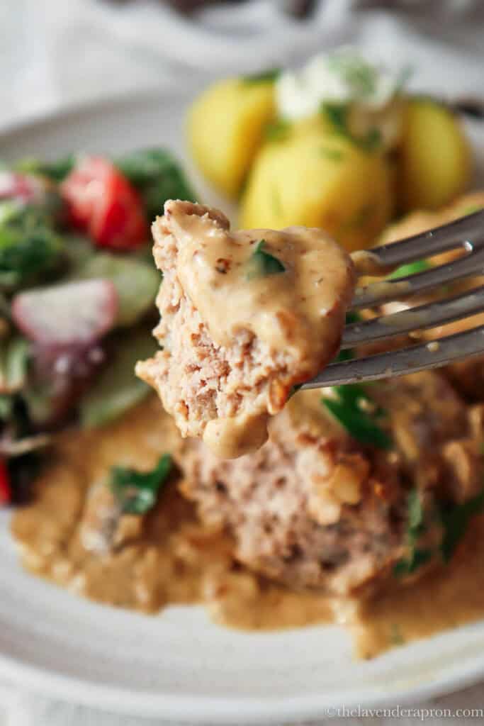 Forkful of juicy Latvian kotlete with creamy sauce.