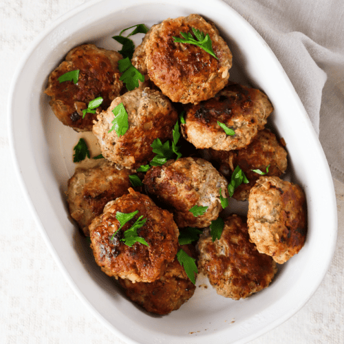 Traditional Latvian Kotletes in a white serving dish with parsley.