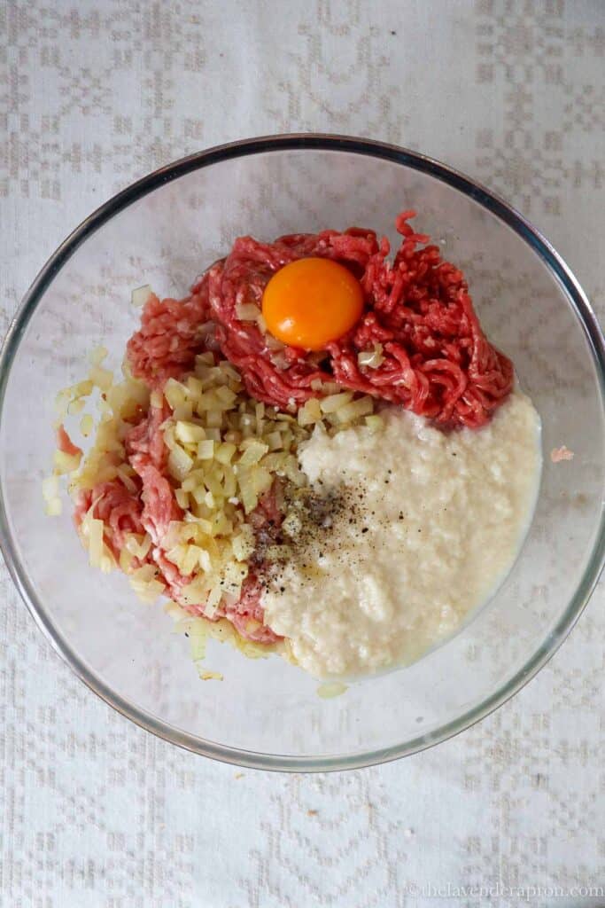 Mixed mince meat with egg, bread, bouillon, salt and pepper in a glass bowl.