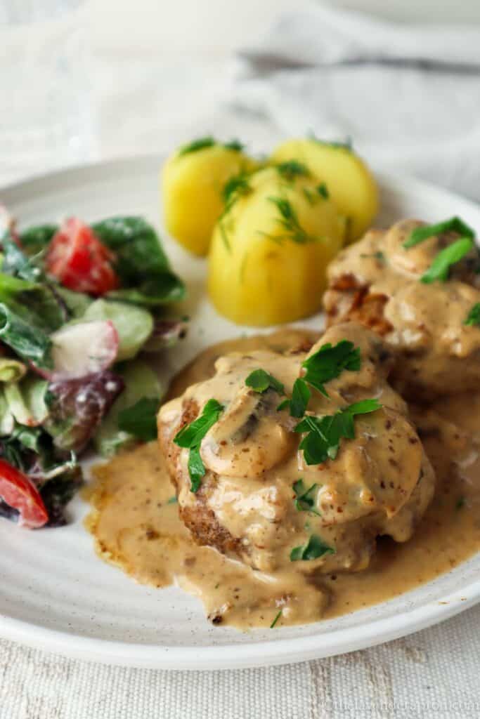 Kotletes served with mushroom cream sauce, boiled potatoes with dill and green salad with cucumbers and tomatoes.