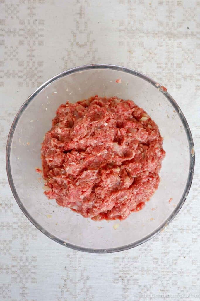 Mixed mince meat with egg, bread, bouillon, salt and pepper in a glass bowl.
