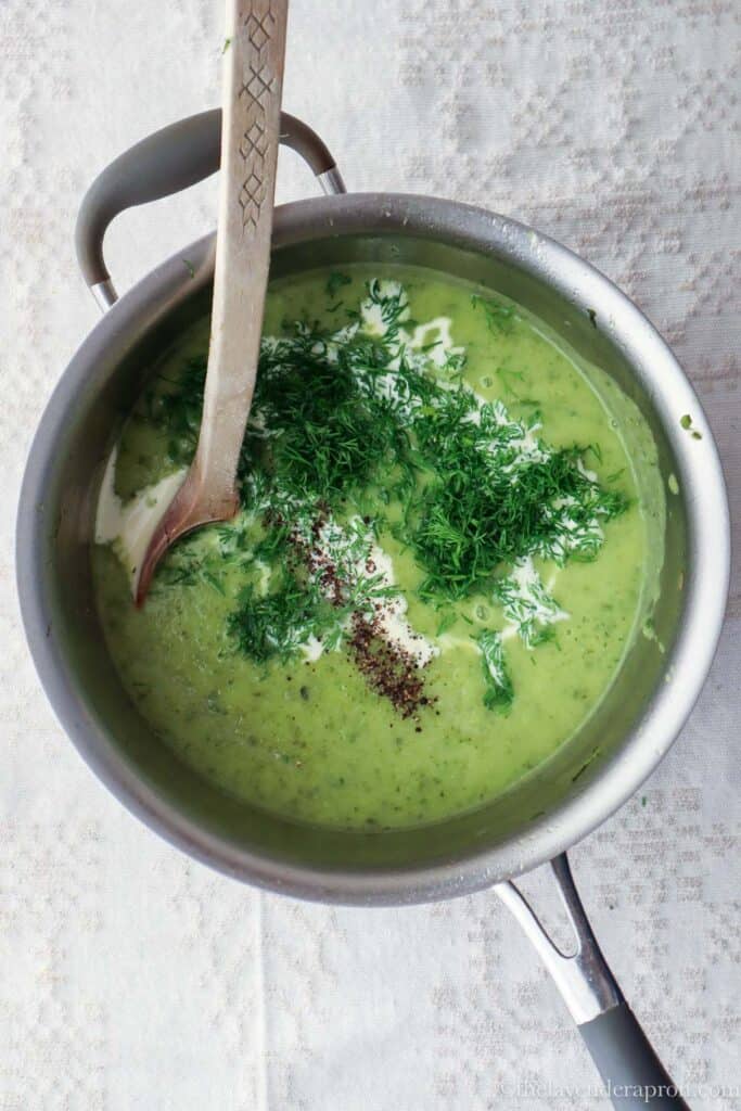 Adding fresh cream, fresh dill, salt and pepper to zucchini soup.