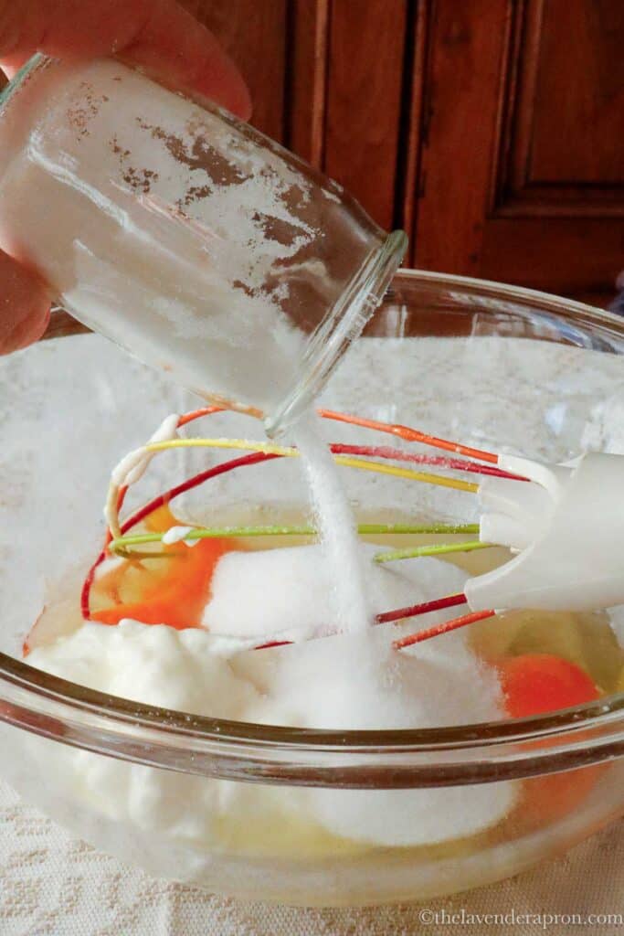 Pouring a yogurt pot full of sugar into a bowl with eggs.