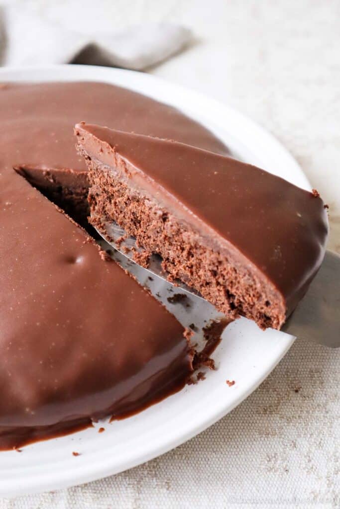 Slice of Belgian chocolate cake cut out of cake covered with chocolate ganache.