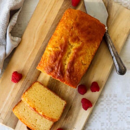 French yogurt cake on a wooden board with slices and raspberries.