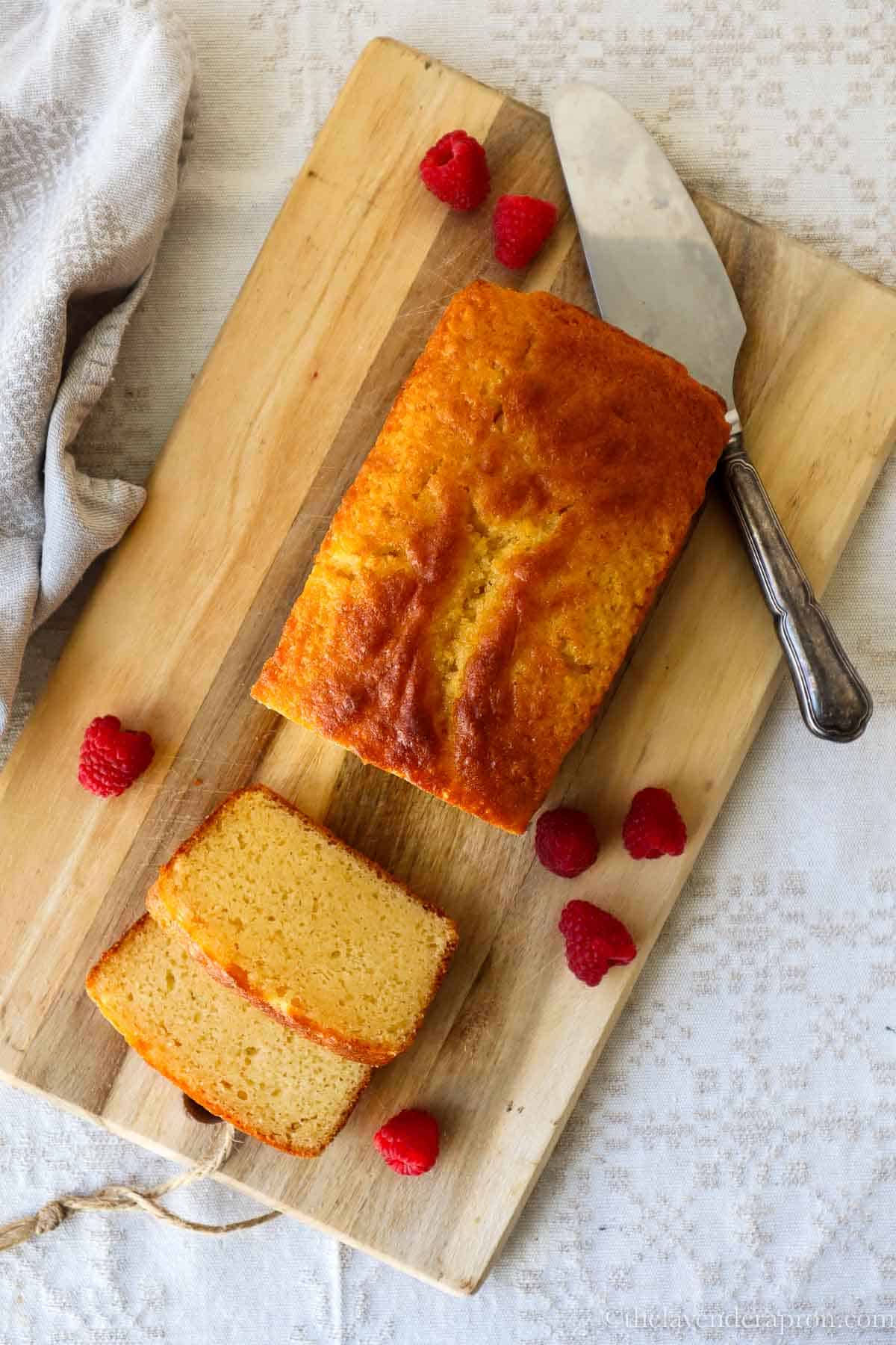 French yogurt cake on a wooden board with slices and raspberries.