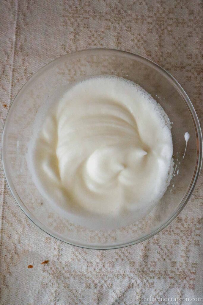 Egg whites whipped into soft peaks in glass bowl.