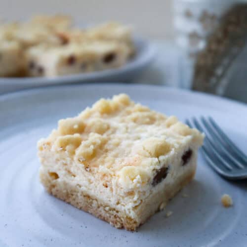 Slice of creamy cottage cheese cheese cake biezpienmaize with platter of cake slices in the background.