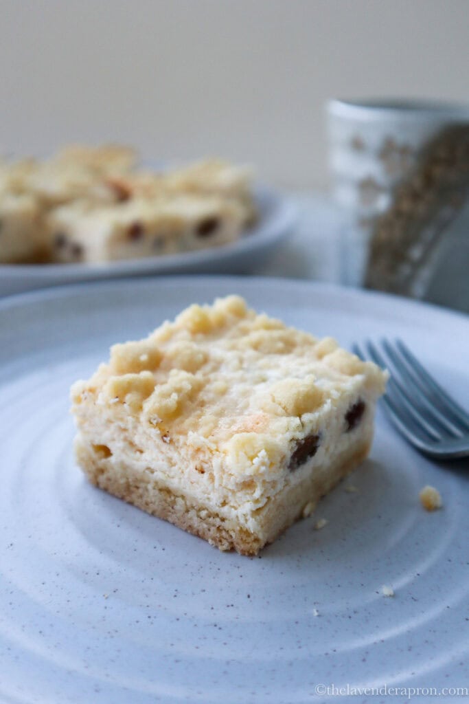 Slice of creamy cottage cheese cheese cake biezpienmaize with platter of cake slices in the background.