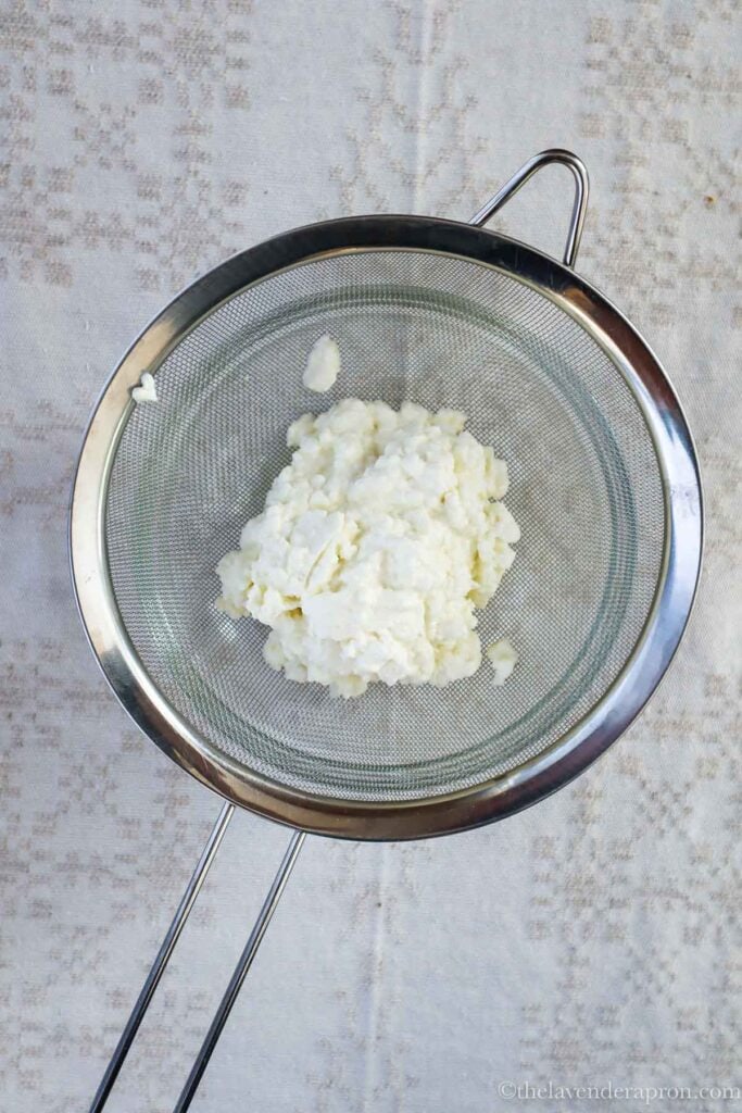 Draining the cottage cheese through a fine mesh sieve.