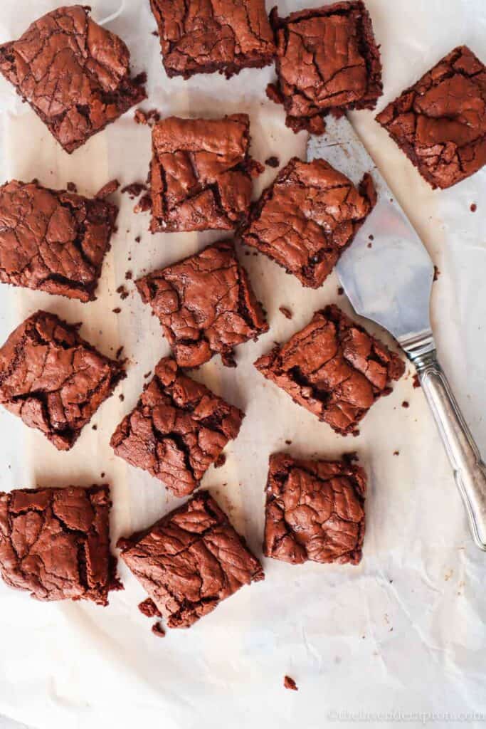Dark chocolate brownies without cocoa powder on parchment paper with a serving spatula.