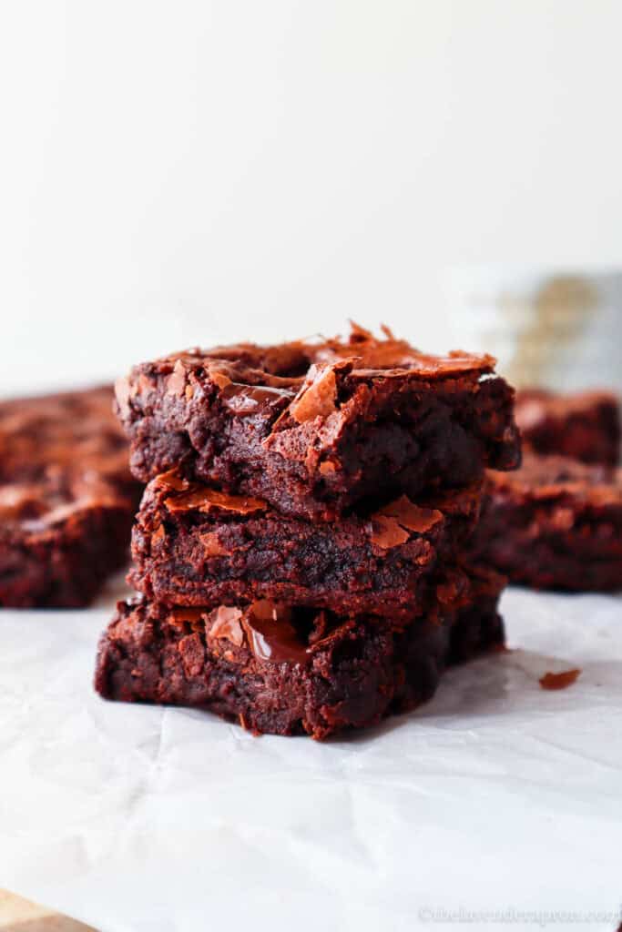 Stack of three very fudgy chocolate brownies without cocoa with crinkly shine top and coffee cup in the background.