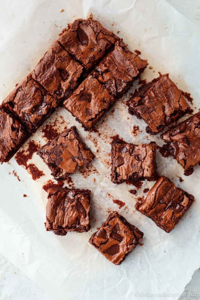 Fudgy chocolate brownies without cocoa powder with chocolate chunks cut into squares on parchment paper.