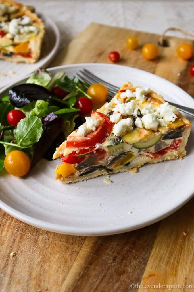 Quiche Provençale with green lettuce and mini tomatoes on small plate.