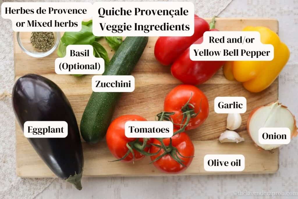 Zucchini, eggplant, tomatoes, onion, garlic, herbs, basil, olive oil, red bell pepper, and yellow bell pepper on a cutting board.