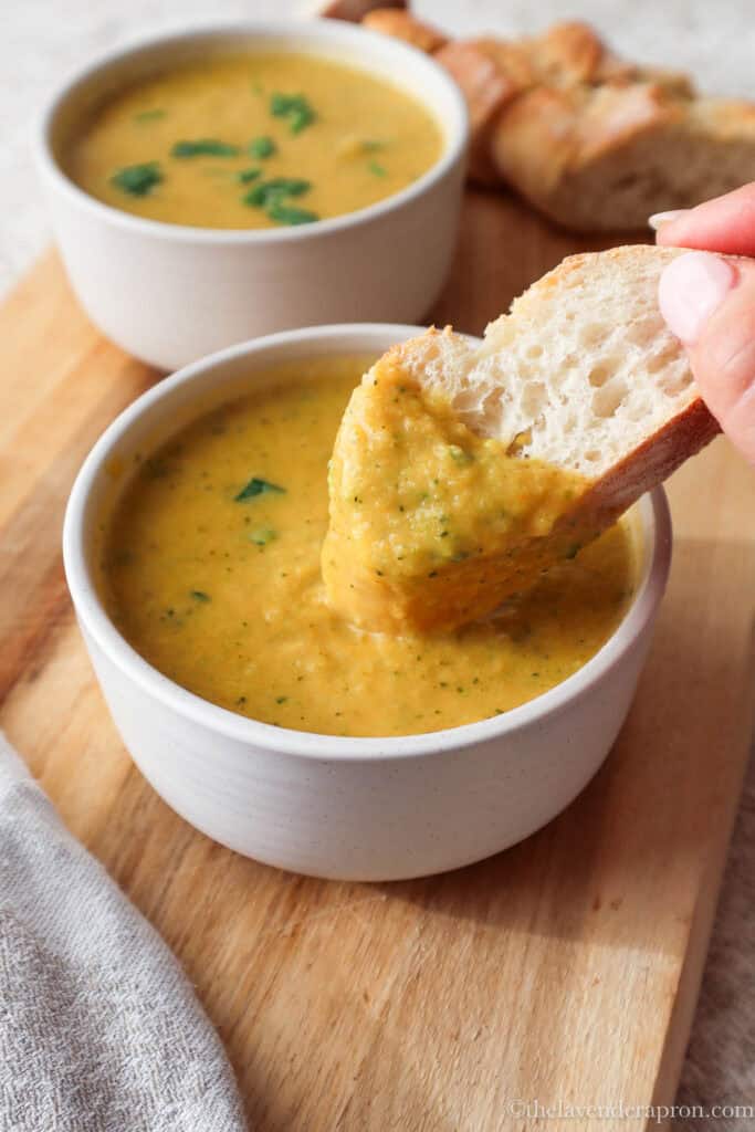 Crusty bread dipped in bowl of broccoli and sweet potato soup.