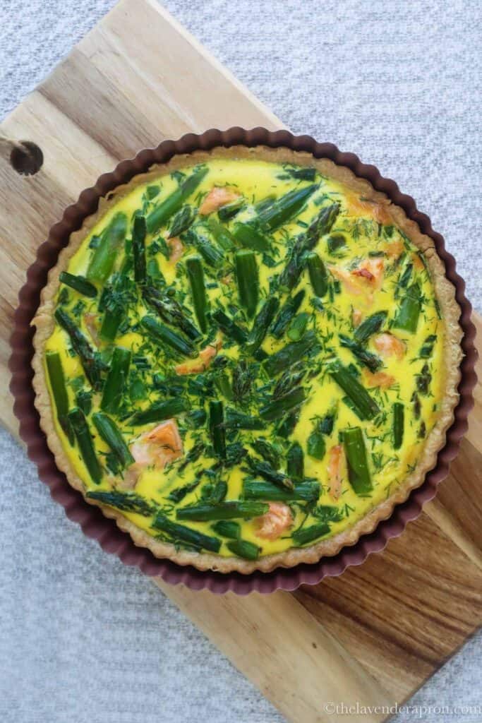 Baked salmon and asparagus quiche on a wooden board.