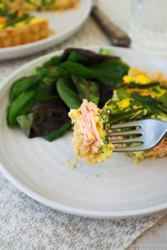 Forkful of salmon and asparagus quiche with large chunks of salmon and bite sized pieces of asparagus.